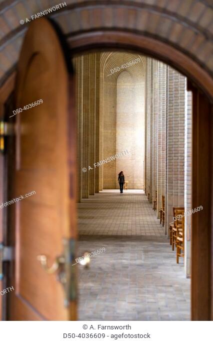 Copenhagen, Denmark woman walks past a votive candle under an arch in the Grundtvig's Church