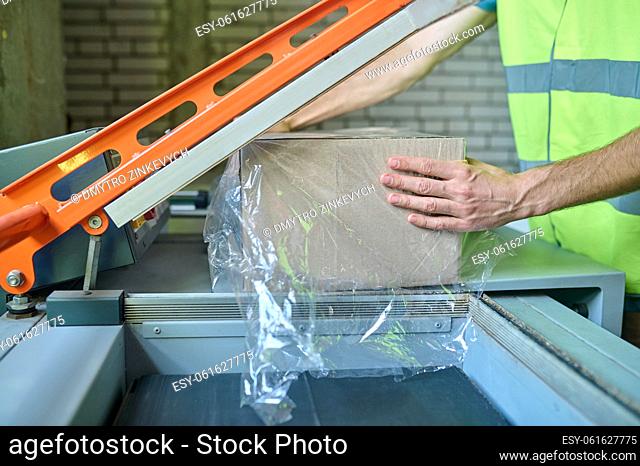 Cropped photo of a storehouse employee placing the cardboard box into the film wrapping machine