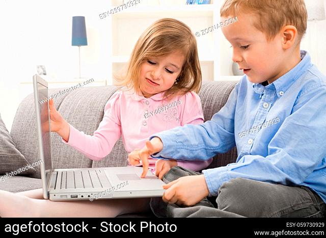 Young children sitting on couch at home with laptop computer. Boy using touch pad, angry girl trying to close teh screen