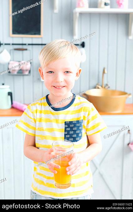 son and young mother in the kitchen eating Breakfast. Boy drinking orange juice. Healthy food concept. holding a glass in his hand