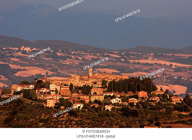 Panoramic view of medieval hilltop town of Monte Castello di Vibio at sunset, with golden light over village and surrounding hills and fields, Umbria, Italy