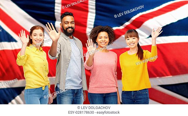 diversity, immigration and people concept - international group of happy smiling men and women waving hands over british flag background