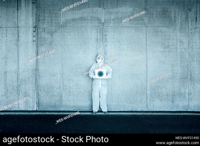 Man wearing protective clothing holding sign with a depiction of a virus