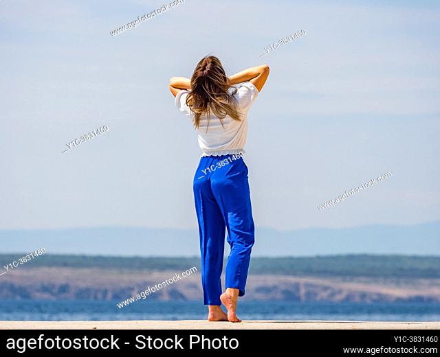 Young woman outside on seaside rearview standing upright fixing her hair