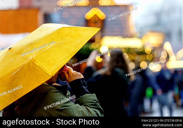 21 December 2023, Hesse, Frankfurt/Main: A woman drinks her mulled wine under an umbrella at the Christmas market in the banking city
