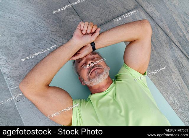 Exhausted mature man resting on exercise mat