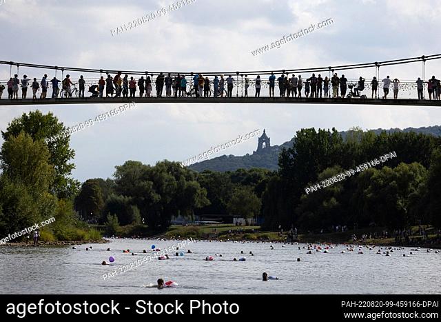 20 August 2022, North Rhine-Westphalia, Minden: Swimmers swimming in the Weser. Spectators stand on the Glacis Bridge. The Kaiser Wilhelm Monument at Porta...