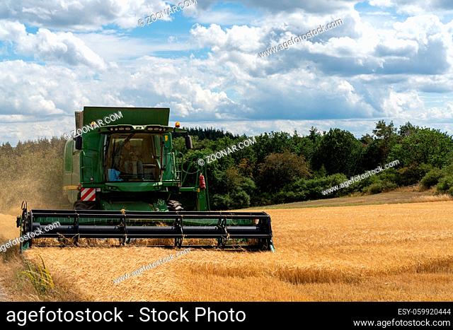 A green combine harvester unloading cut wheat crop into a tractor trailer