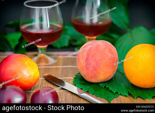 Still life: on the table on the green leaves are fruits, next to two glasses of wine