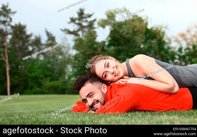 Picture of happy sport man and woman resting on green grass in park. Beautiful couple spending their weekends with nature