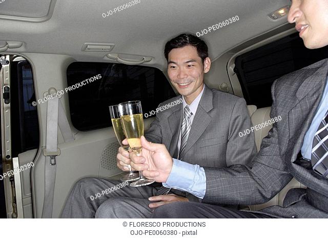 Two businessmen in limousine toasting champagne flutes