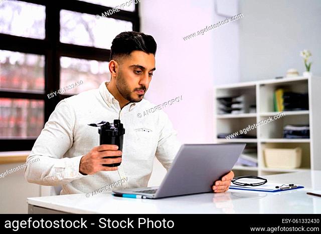 Protein Shake On Desk And Man In Foreground Using Computer
