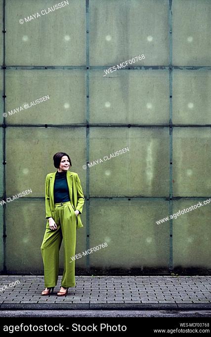 Elegant businesswoman wearing green suit standing at a wall