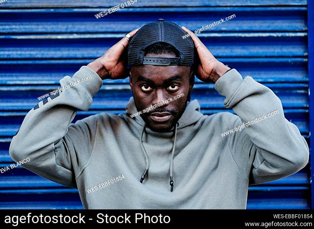 Confident young man wearing cap against blue corrugated wall