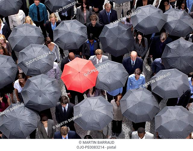 Red umbrella standing out in crowd of business people