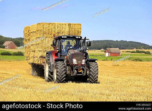 Transporting straw bales with Valtra tractor and agricultural trailer from harvested field to storage in late summer. Salo, Finland. August 16, 2020