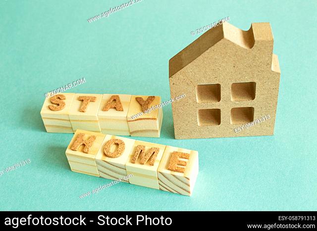 House model and word 'Stay Home' wooden blocks on green background. Rest, Self Quarantine, Virus prevention concept