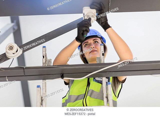 Young female electrician installing lamp