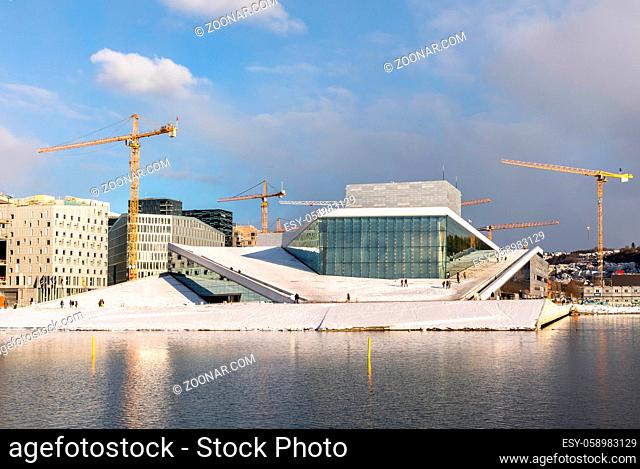 Oslo, Norway, March 2018: The Opera House in Oslo in winter, surrounded by cranes. The Oslo Fjord in front