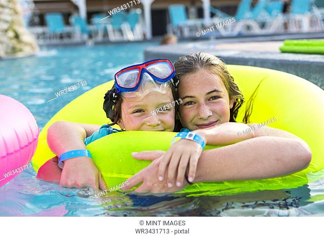 siblings playing in pool with colorful floaties