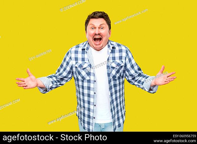 Portrait of surprised handsome middle aged businessman in casual checkered shirt standing with raised arms, looking at camera with unbelievable amazed face