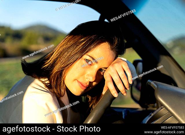 Young woman leaning on steering wheel during sunset