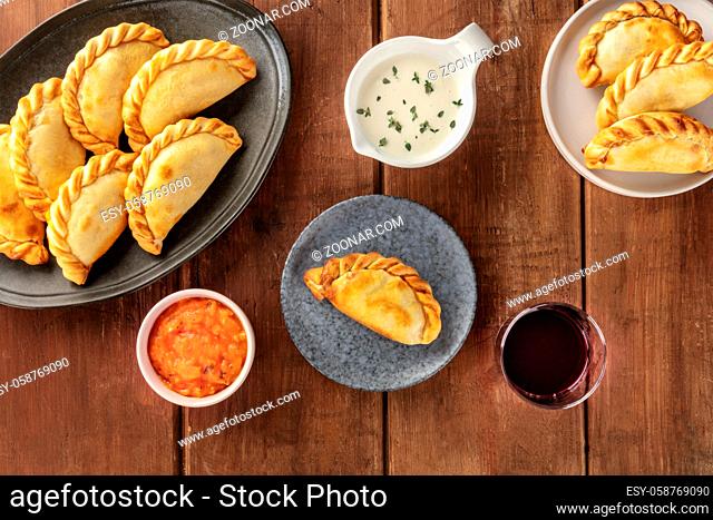 Empanadas with sauces and wine, shot from above on a dark rustic wooden background