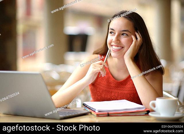 Happy student with laptop and notebook dreaming looking at side in a restaurant terrace