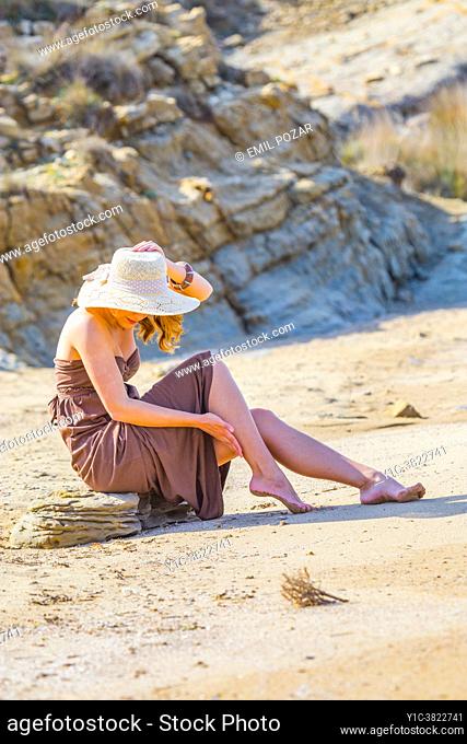 Teen girl barefeet on sandy beach sitting on stone