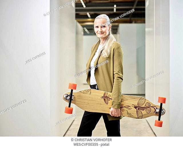 Portrait of businesswoman carrying longboard on office floor