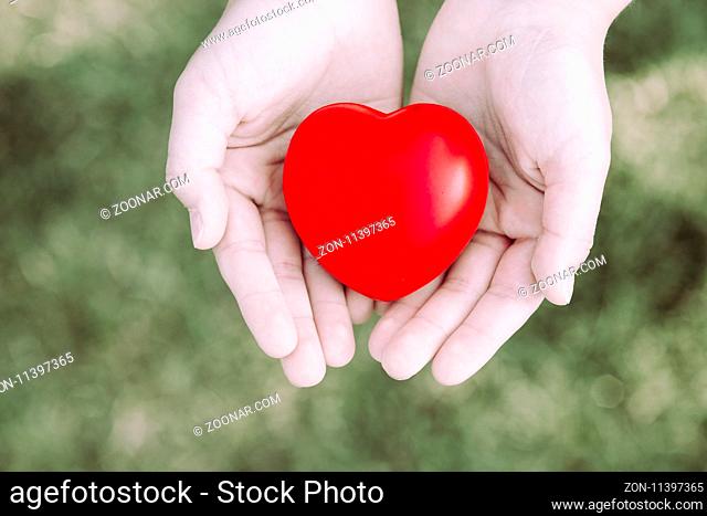 Female hands giving red heart on blurred background - safety concept - retro toned vintage image