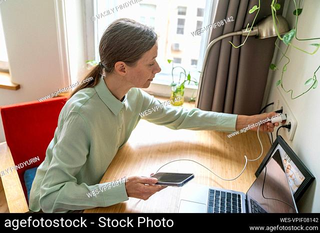 Freelancer plugging in mobile phone charger at home