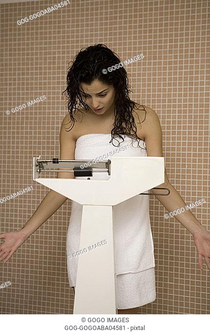 Woman wrapped in a towel weighing herself