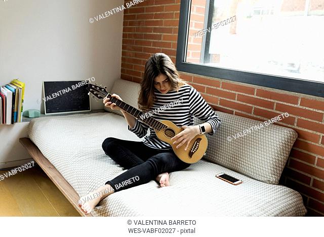 Young woman sitting on couch at home playing guitar