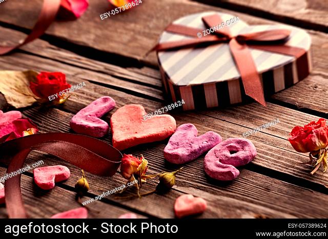 Word Love with heart shaped Valentines Day gift box on old vintage wooden plates. Sweet holiday background with rose petals and dried rose flowers