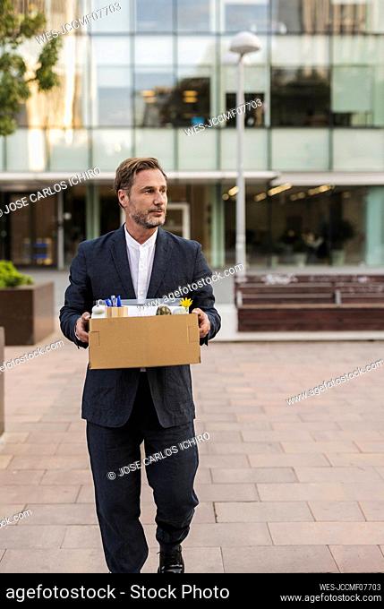 Businessman carrying cardboard box in front of office building