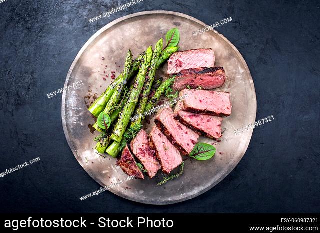 Barbecue dry aged wagyu roast beef steak with green asparagus and lettuce offered as top view on a rustic modern design plate
