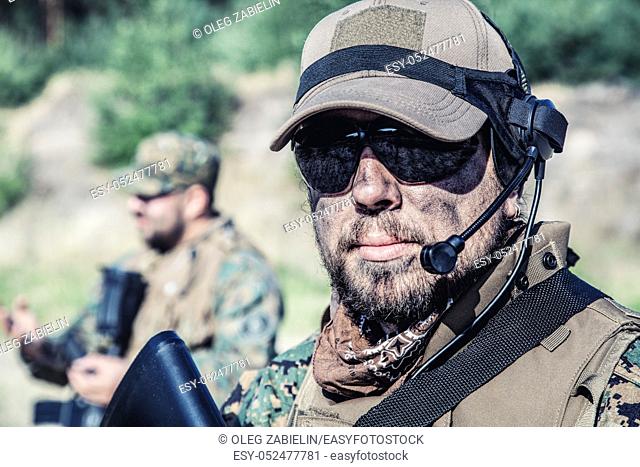Location shot of United States Marine with rifle weapons in uniforms. Military equipment, army helmet, warpaint, smoked dirty face, tactical gloves