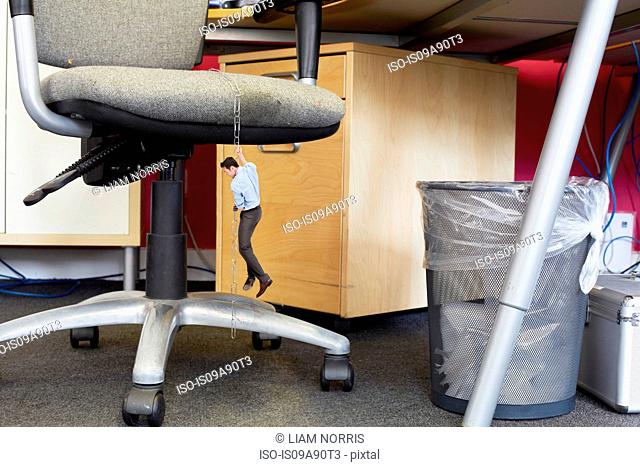 Businessman climbing down large paper clips on oversized office chair