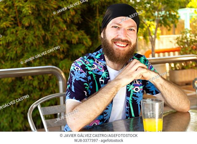portrait of happy young man with beard and headscarf while having a soda on a terrace