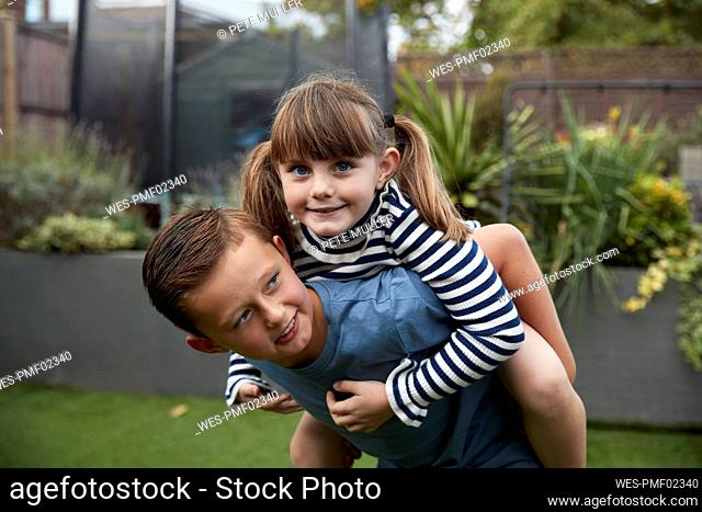 Smiling boy giving piggyback ride to sister in garden