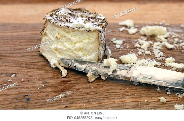 Close up one cut fresh French artisan gourmet goat cheese with herb spices and knife on wooden cutting board, high angle view