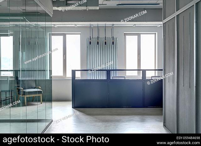 Business interior in a loft style with gray walls. There is a blue metal reception rack with two armchairs on the windows background