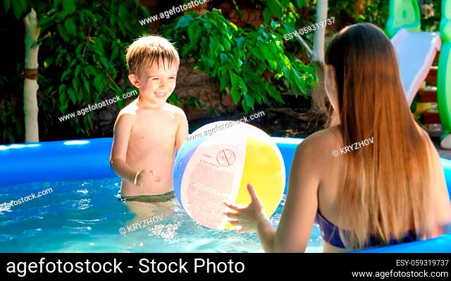 Happy laughing mother with little son playing with colorful beach ball in swimming pool. Family summer vacation and holidays