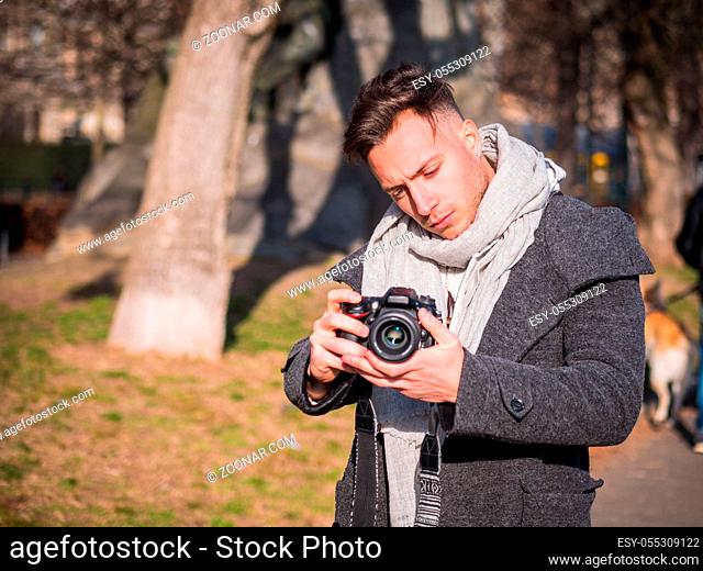 Handsome young male photographer or videomaker filming video footage with professional videocamera, outdoor in city park