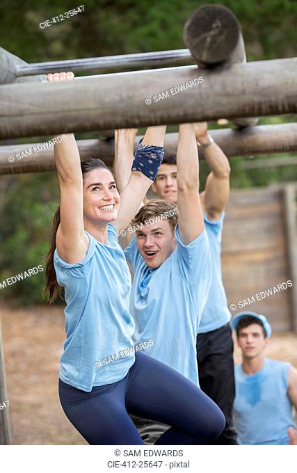 Smiling woman crossing monkey bars on boot camp obstacle course