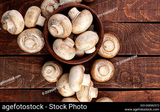 Heap of mushrooms, champignons in wooden bowl on brown background, top view