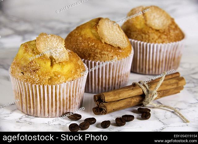 three delicious cupcakes, coffee grains and cinnamon sticks on marble background