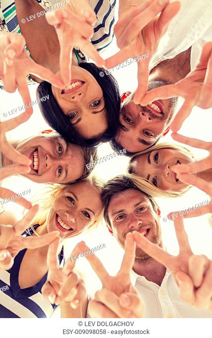 friendship, happiness and people concept - smiling friends in circle showing victory sign