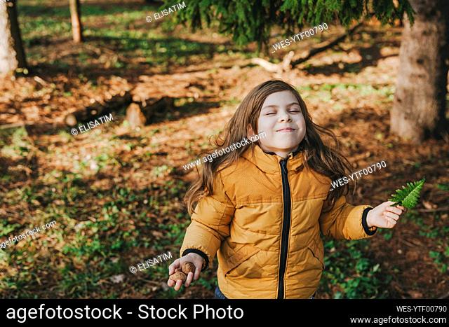 Playful girl holding nuts and fern in forest